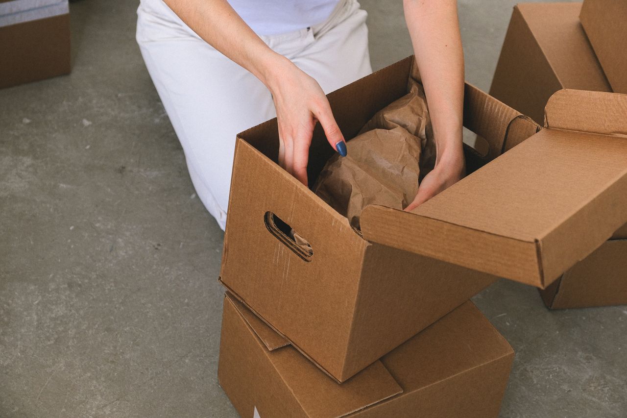 Services From above of crop anonymous relocating female packing wrapped items into carton box while preparing for moving to new apartment