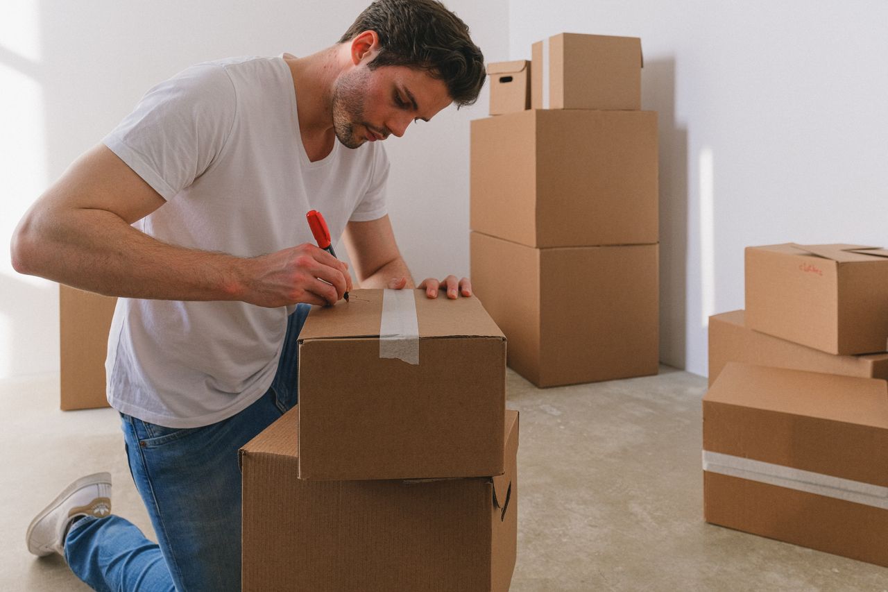 Services A man labels cardboard boxes for moving, kneeling indoors with natural light.