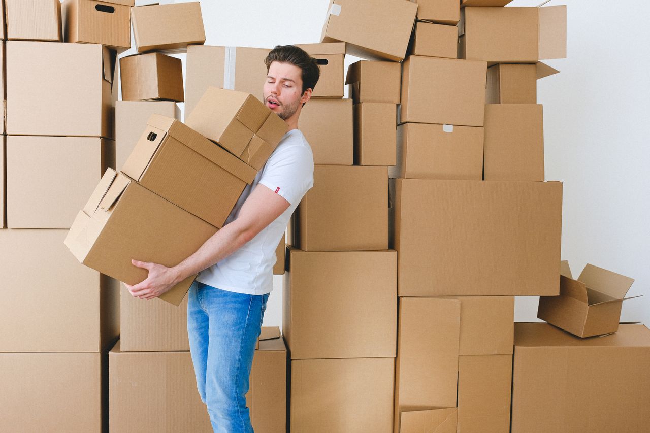 Young unshaven guy in casual clothes carrying stack of heavy cardboard boxes during relocation into new apartment